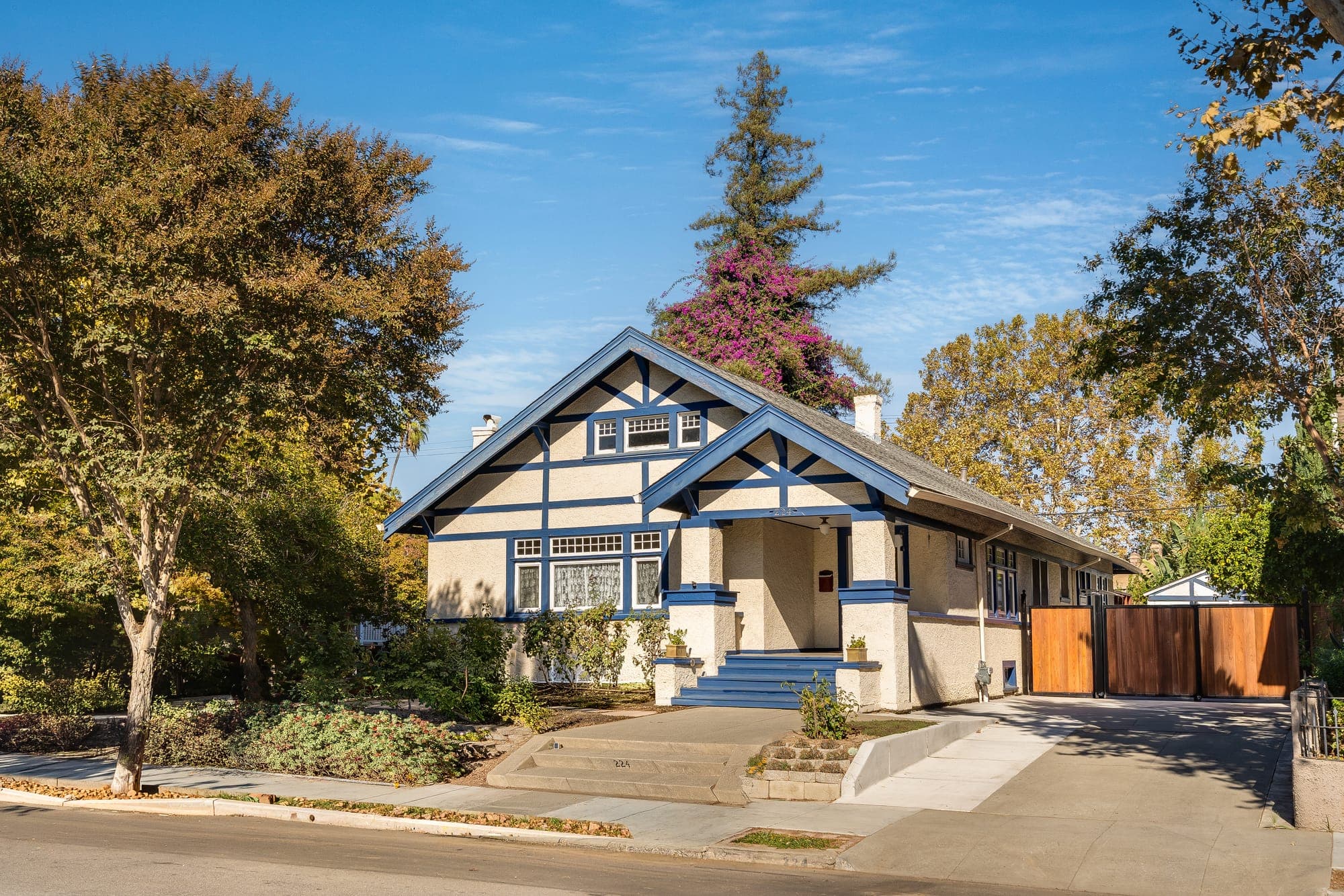 The front of the home on a clear day: twin gables, blue trim, and steps rising to the porch.