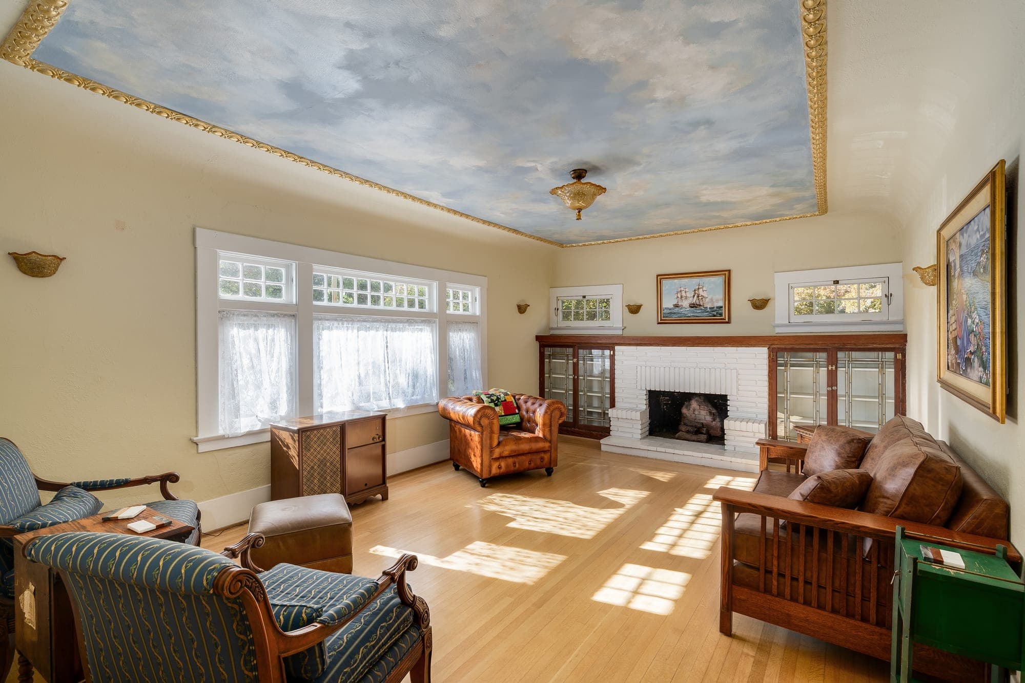 The living room in afternoon light, with a painted sky ceiling and a white brick fireplace.