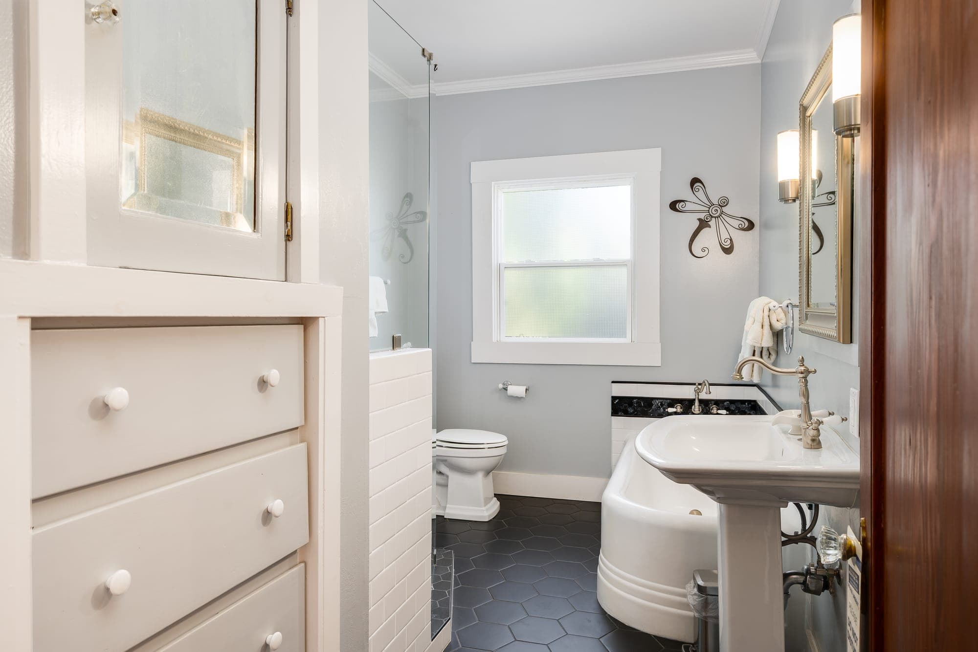 A bathroom with a pedestal sink, soaking tub, and hexagon tile floor.
