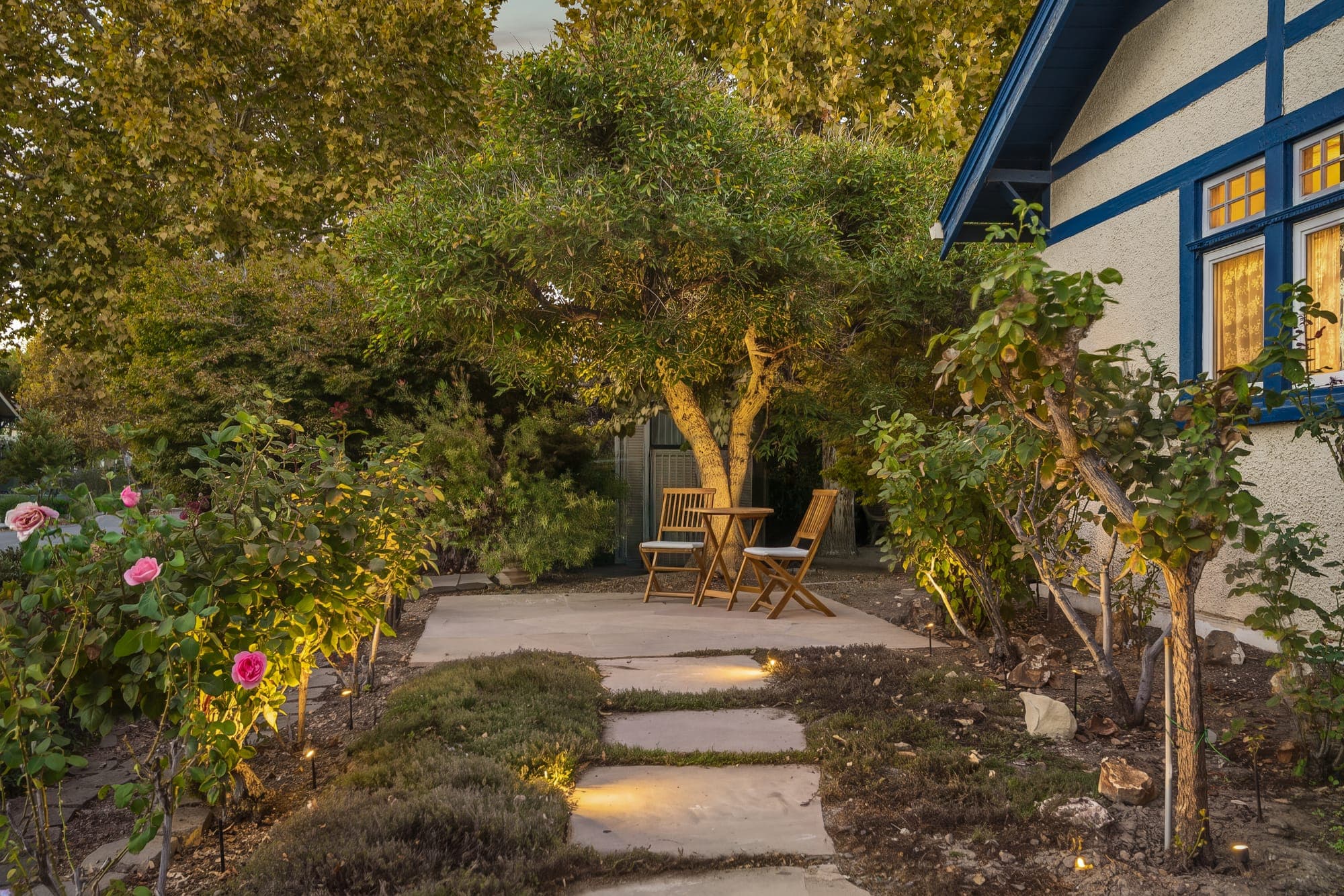 A lit path through the side garden to a bistro table under the trees.